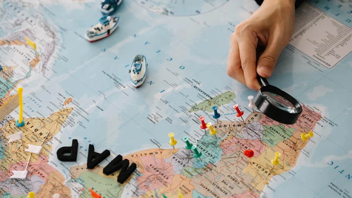 Hand using magnifying glass over map with pins
