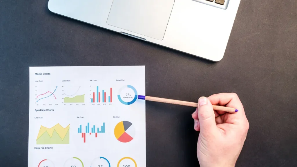 Printed analytics charts with a hand pointing near a laptop
