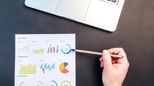 Printed analytics charts with a hand pointing near a laptop